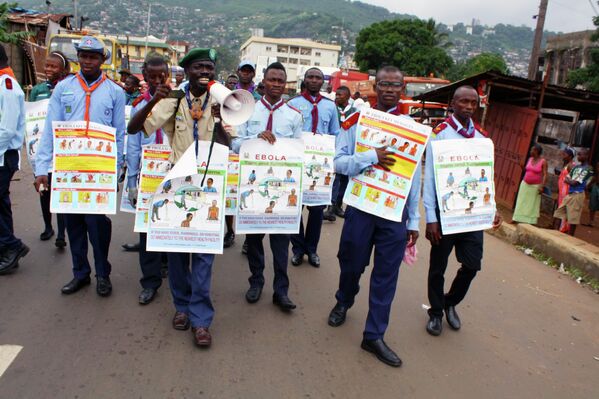Члены ЮНИСЕФ несут плакаты с описанием симптомов заражения вирусом эбола