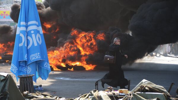 Священнослужитель идет мимо подожженных покрышек на площади Независимости в Киеве. Архивное фото.