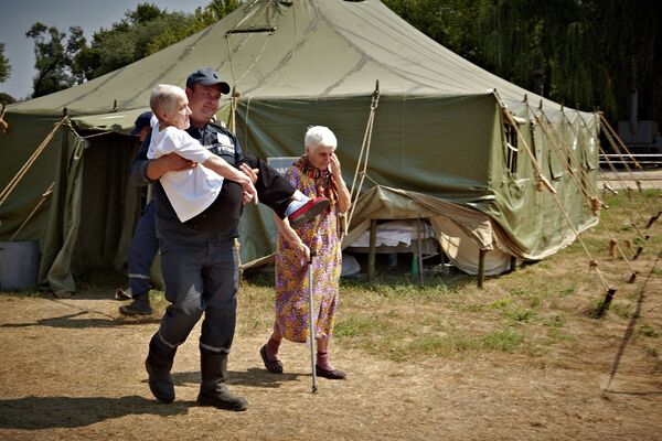 Сотрудник МЧС Украины переносит пожилую женщину, приехавшую из зоны силовой операции киевских властей на востоке Украины