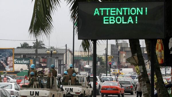 Конвой ООН проезжает мимо экрана, отображающего сообщение об Эболе на улице в Абиджане