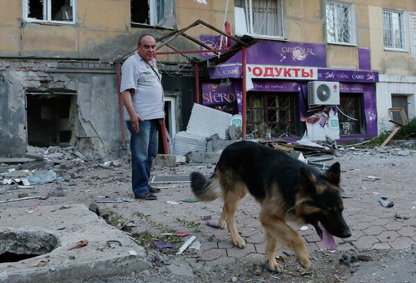Мужчина с собакой рядом с поврежденным в результате обстрела зданием в Донецке
