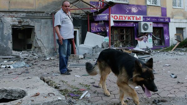 Мужчина с собакой рядом с поврежденным в результате обстрела зданием в Донецке
