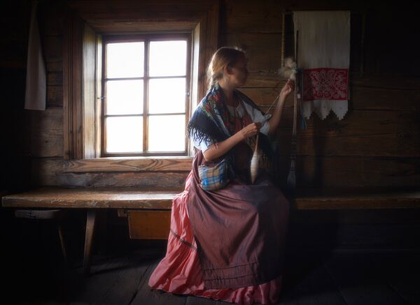 Женщина в национальной одежде прядет пряжу в музее-заповеднике Кижи