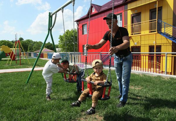 Отец играет с детьми возле здания детского сада №26 в Введенском районе Чечни