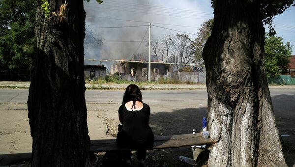 Женщина сидит напротив своего дома сгоревшего в результате обстрела в Донецке