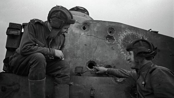 Два советских танкиста сидят на броне подбитого танка во время Великой Отечественной войны. Архивное фото