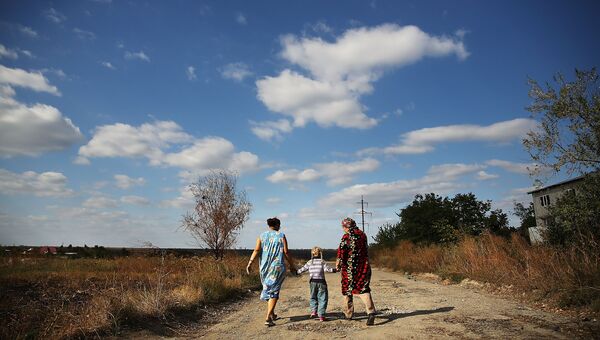 Девочка, ее мама и бабушка идут по разбитой дороге на окраине Луганска