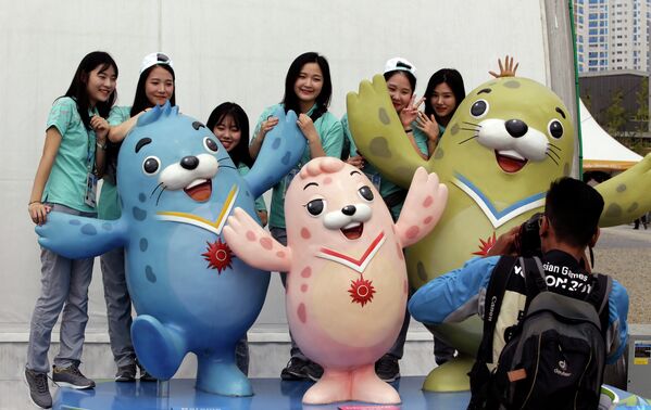 Волонтеры позируют с тремя официальными талисманами 17-ых Азиатских игр в Южной Корее