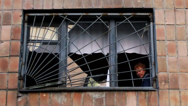Женщина смотрит из окна своего дома, разрушенного после обстрела украинскими силовиками в Донецке