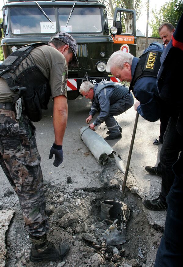 Спасатели и ополченцы достают из земли осколки снаряда после обстрела Донецка
