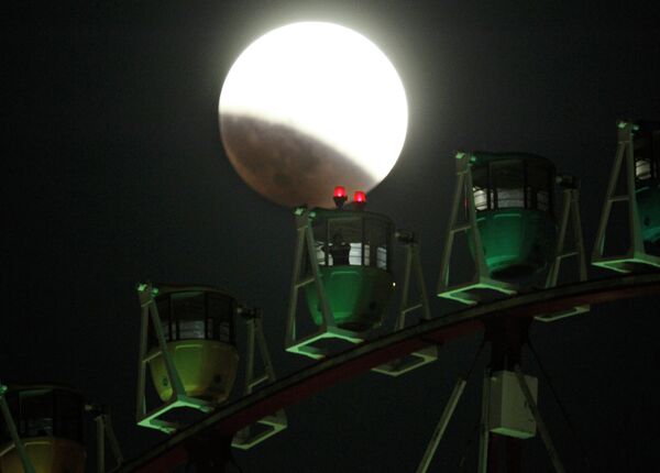 Люди катаются на колесе обозрения во время полного лунного затмения в Токио 8 октября 2014