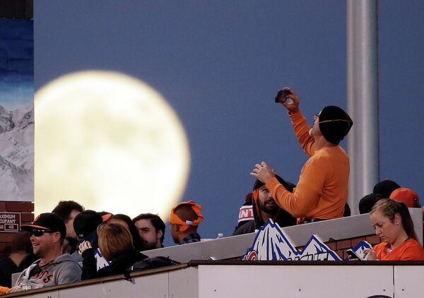 Болельщик фотографирует полную луну во время бейсбольного матча в Сан-Франциско 7 октября 2014 года