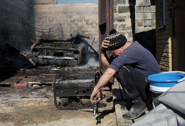 Александр сидит возле своей сгоревшей машины и, разрушенного в результате боев за аэропорт Донецка, дома. 7 октября 2014