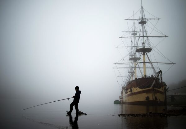 Мальчик ловит рыбу на фоне фрегата Флагман в Великом Новгороде