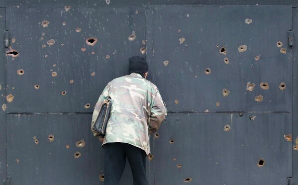 Человек смотрит через пулевые отверстия в воротах дома, после обстрела села Спартак, на окраине Донецка