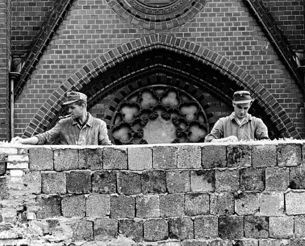 Восточногерманские рабочие кладут на построенную стену куски битого стекла