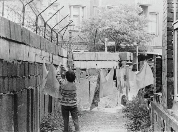 Женщина развешивает белье во дворе жилого дома примыкающего к Берлинской стене
