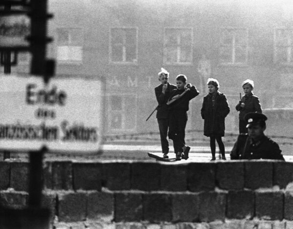 Подростки из Восточного Берлина идут вдоль Берлинской стены с игрушечным оружием