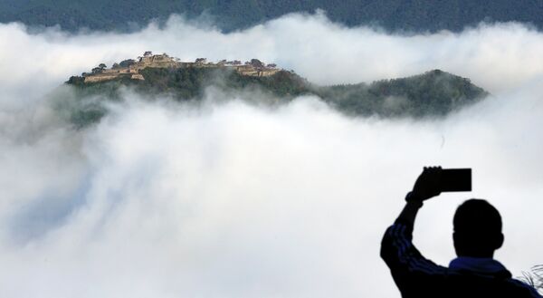 Турист фотографирует как утренний туман покрывает замок Такэда