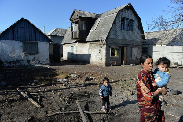 Женщина с детьми у своего дома, пострадавшего в результате артиллерийского обстрела