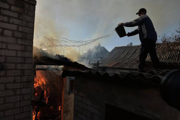 Житель Донецка тушит горящий огонь в доме, пострадавшем во время артиллерийского обстрела