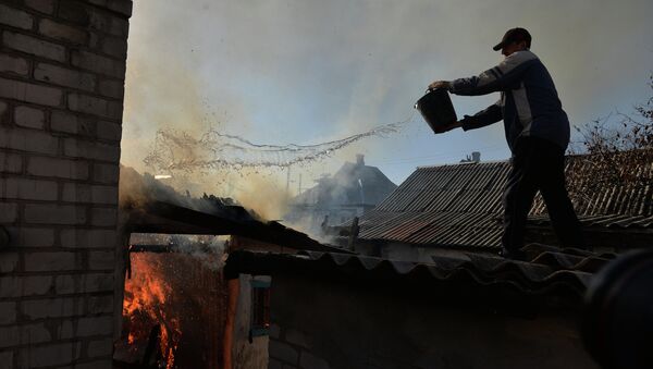 Житель Донецка тушит горящий огонь в доме, пострадавшем во время артиллерийского обстрела. Архивное фото