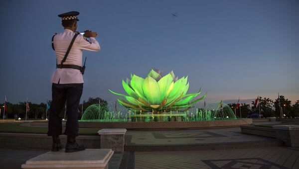 Полицейский на посту снимает на мобильный телефон фонтан в виде цветка лотоса в Нейпьидо, Мьянма