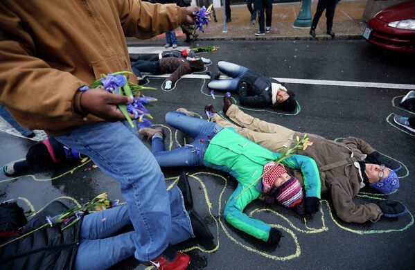 Люди лежат на земле в очерченных мелом контурах во время акции протеста по случаю 100-й день смерти Майкла Брауна