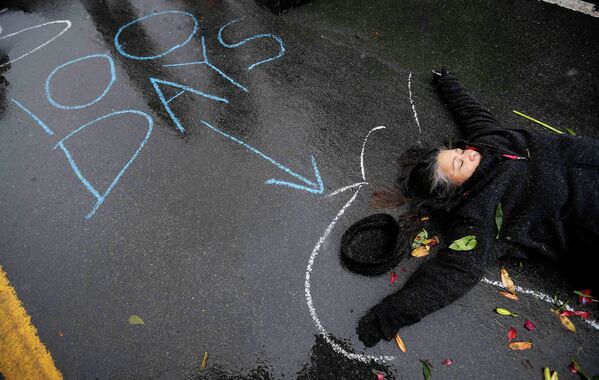 Женщина лежит на земле в очерченных мелом контурах во время акции протеста по случаю 100-й день смерти Майкла Брауна