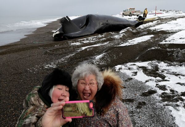 Жители Аляски фотографируются на фоне выловленного кита на берегу в Барроу