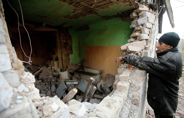 Мужчина рядом с разрушенным в результате обстрела домом в поселке Красный Пахарь
