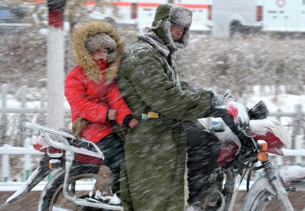 Взрослый с ребенком едут на мотоцикле несмотря на сильный ветер и снег в Китае