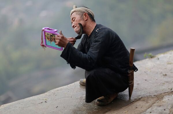 Человек из племени мяо бреется с серпом, утром в селе Баша в провинции Гуйчжоу