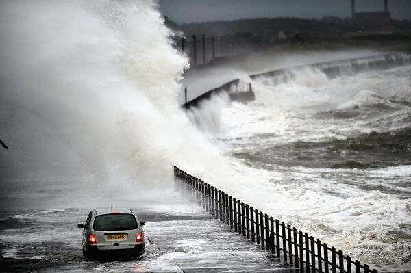 Автомобиль проезжает мимо разбивающихся о набережную волн во время штормового предупреждения в Шотландии