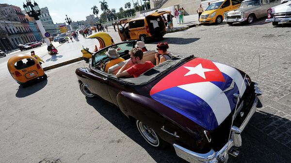 Туристы катаются на классическом американском кабриолете с кубинским национальным флагом в Гаване, Архивное фото