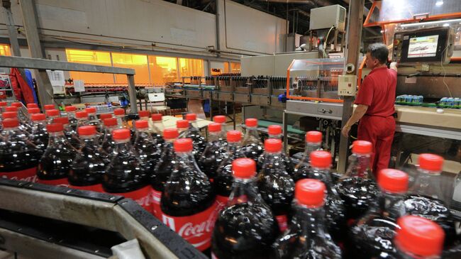 Сотрудник завода Coca-Cola работает на линии розлива продукции в пластиковую тар