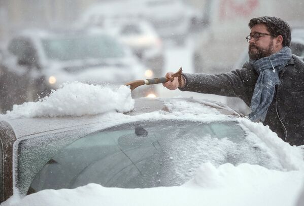 Автовладелец счищает снег с автомобиля в Москве