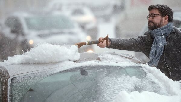 Автовладелец счищает снег с автомобиля в Москве
