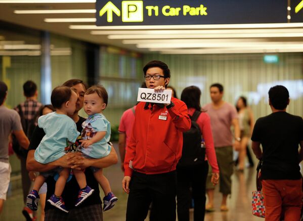Сотрудник аэропорта Чанги держит табличку с номером пропавшего рейса QZ8501 компании Air Asia
