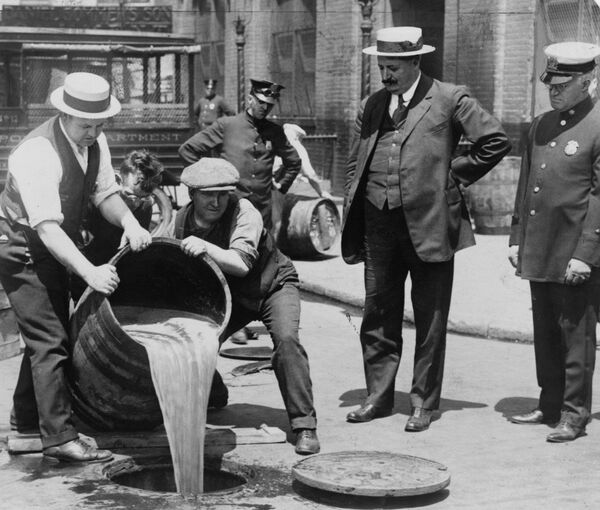 Инспекторы сливают баррель конфискованного пива в канализацию во время действия сухого закона в Америке