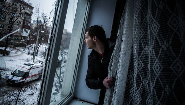Мужчина смотрит через окно квартиры, поврежденной в результате артобстрела Донецка