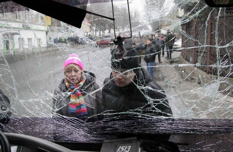 Люди смотрят через лобовое стекло обстрелянного троллейбуса в Донецке