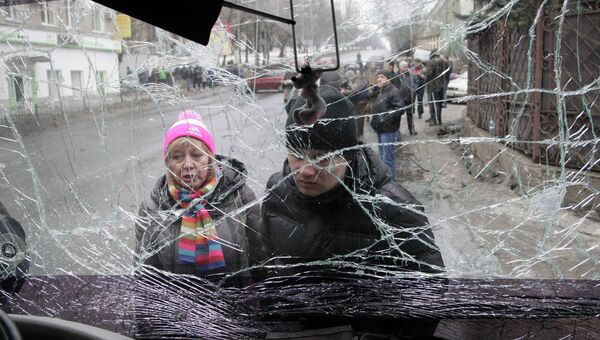 Люди смотрят через лобовое стекло обстрелянного троллейбуса в Донецке