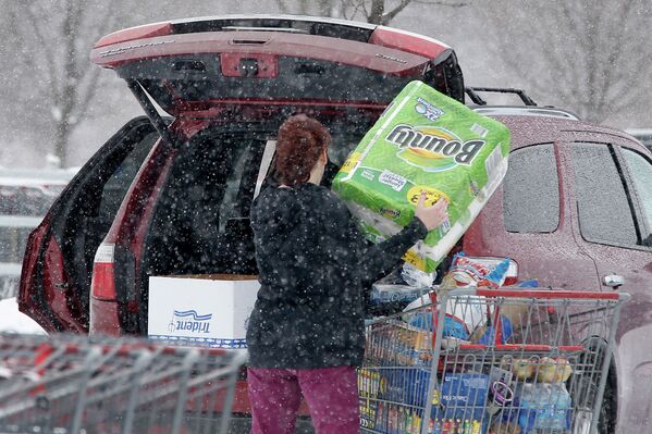 Женщина убирает покупки в багажник своего автомобиля во время снегопада в штате Пенсильвания, США