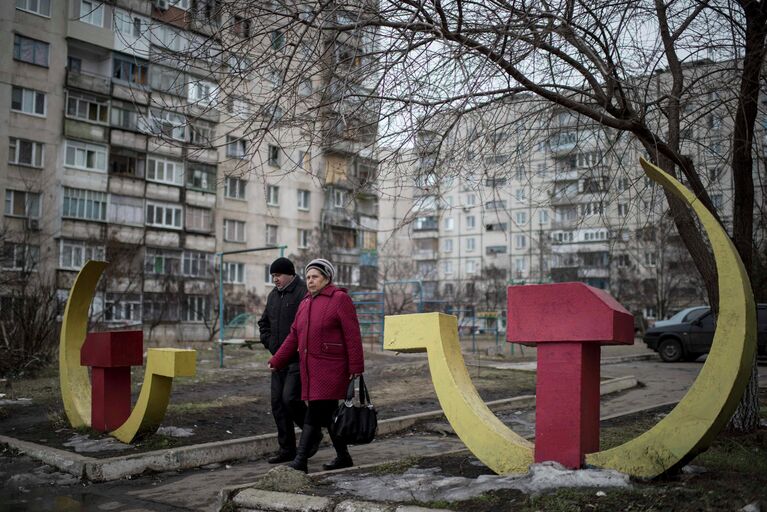 Местные жители проходят мимо скульптур серпа и молота в Мариуполе, Украина