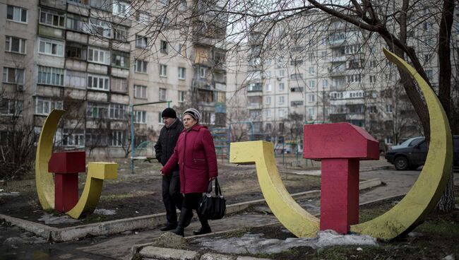 Местные жители проходят мимо скульптур серпа и молота в Мариуполе, Украина