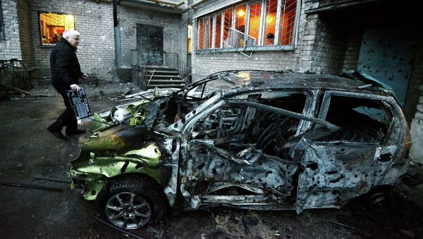 Сгоревшая автомашина у пострадавшего от обстрела жилого многоэтажного дома в Донецке
