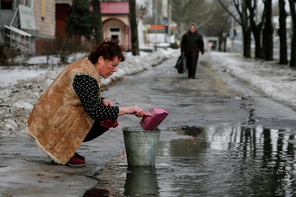 Женщина набирает воду из лужи на улице в Донецке