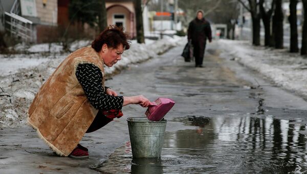 Женщина набирает воду из лужи на улице в Донецке