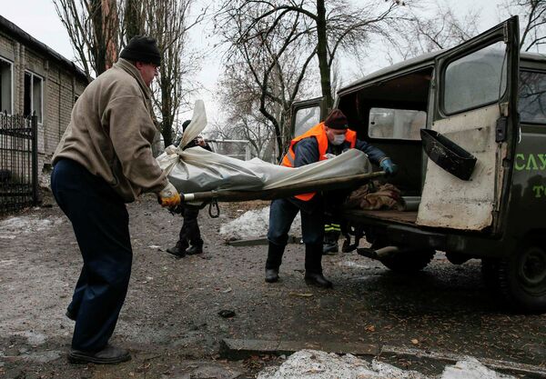 Люди грузят в автомобиль тело убитого в результате обстрела жителя Донецка